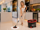 Mulher utilizando o mop giratório The Black Tools TBBL04 para limpar piso de cozinha, com o balde centrífuga vermelho e preto ao lado