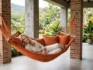 Mulher relaxando em uma rede de descanso de casal em uma varanda aconchegante, cercada por plantas e natureza.