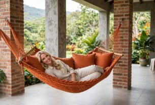 Mulher relaxando em uma rede de descanso de casal em uma varanda aconchegante, cercada por plantas e natureza.